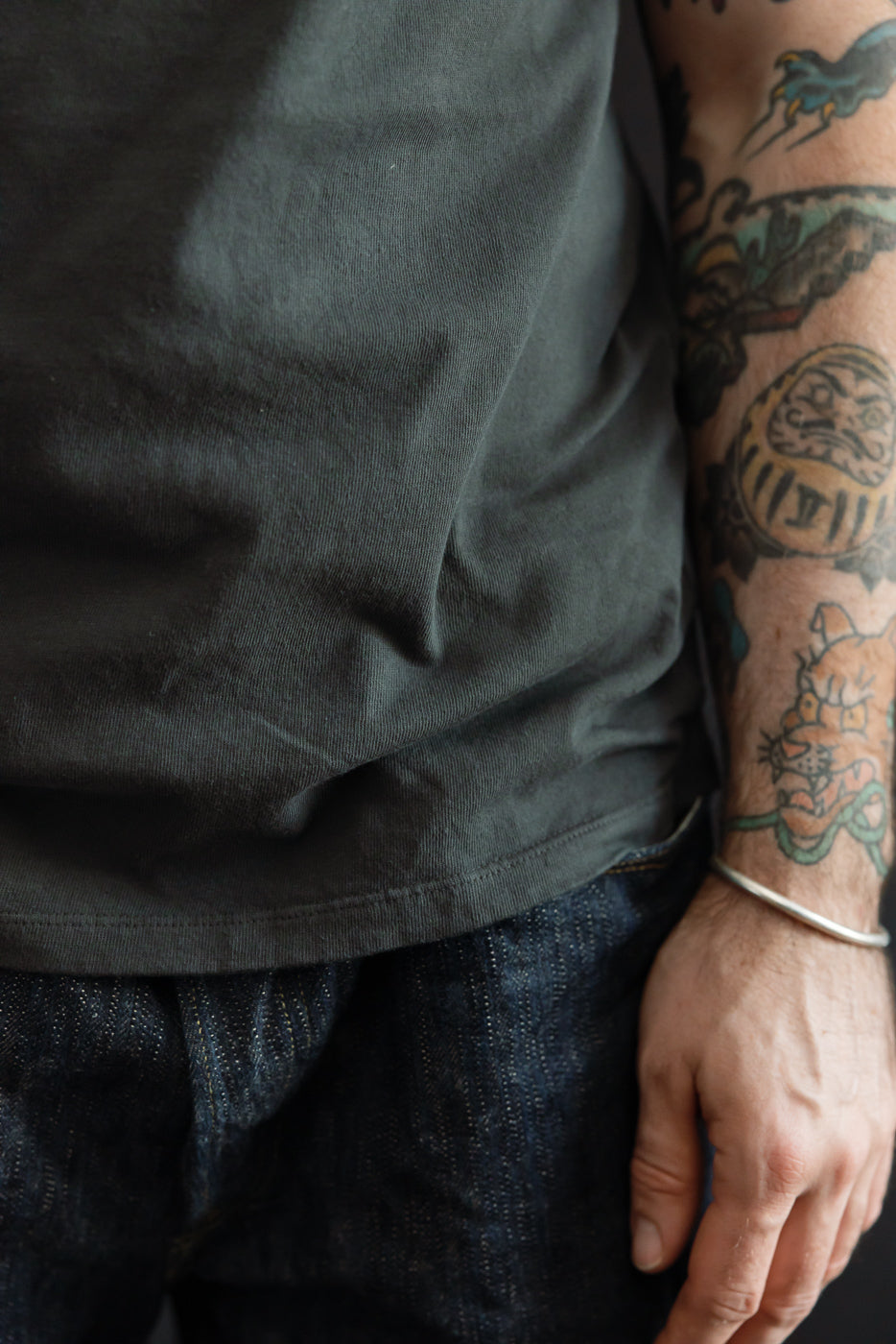Close-up side view of male model's torso in dark tee, showing hem detail and selvedge denim, athletic build