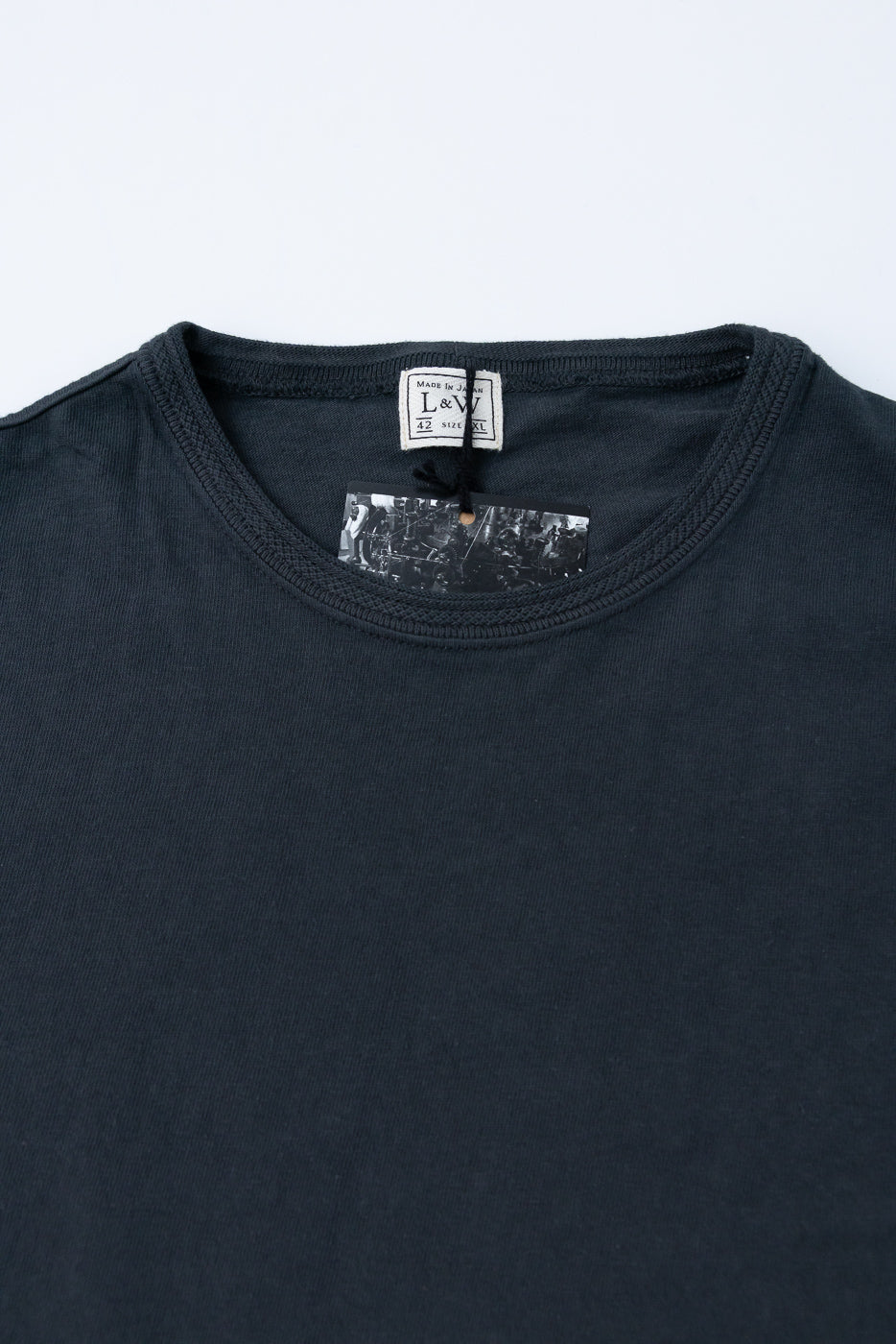 Close-up front view of dark tee showing L&W tag, ribbed crew neck, and fabric texture. Made in Japan, size XL.