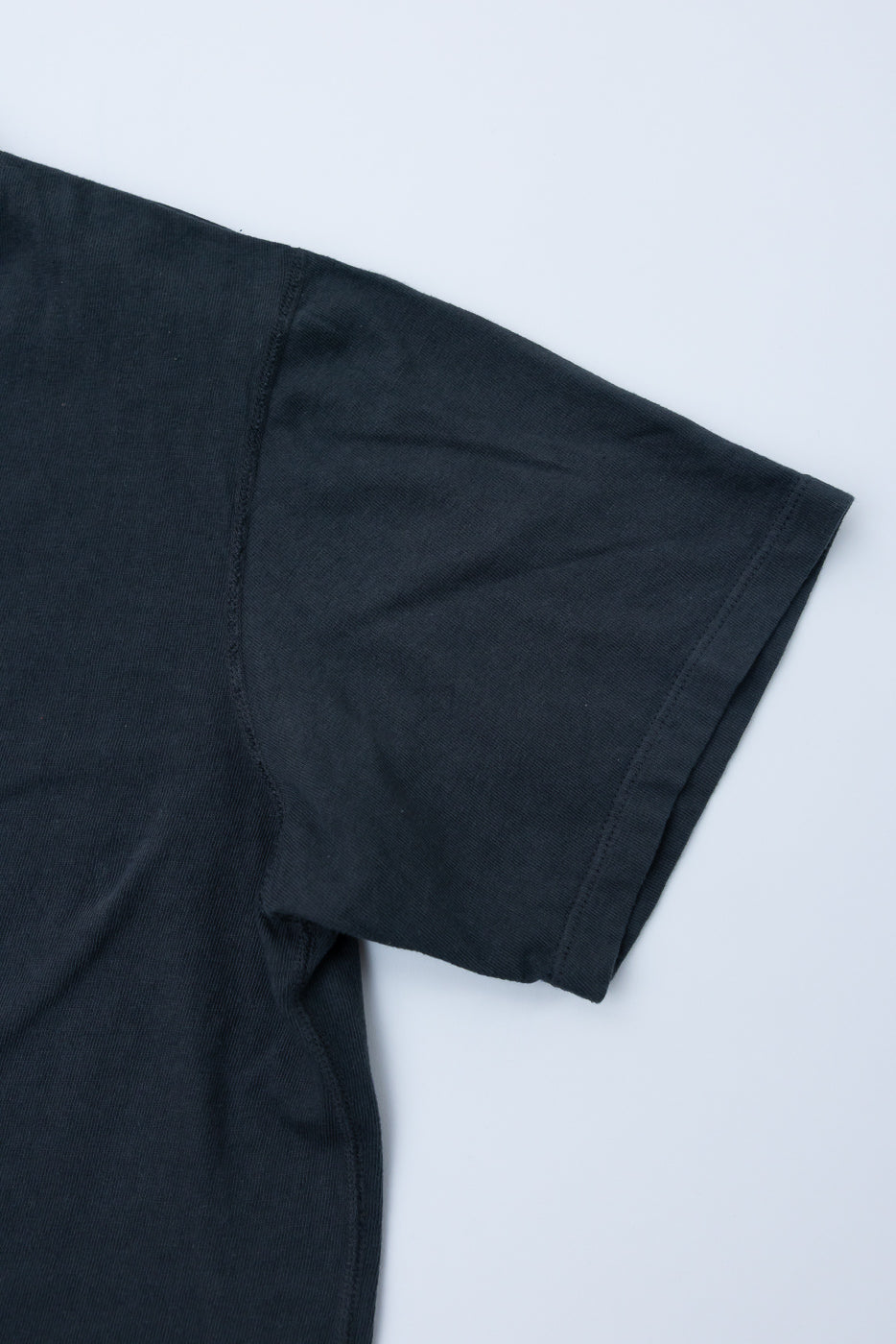 Close-up front view of black t-shirt sleeve, showing ribbed texture and clean hem stitching