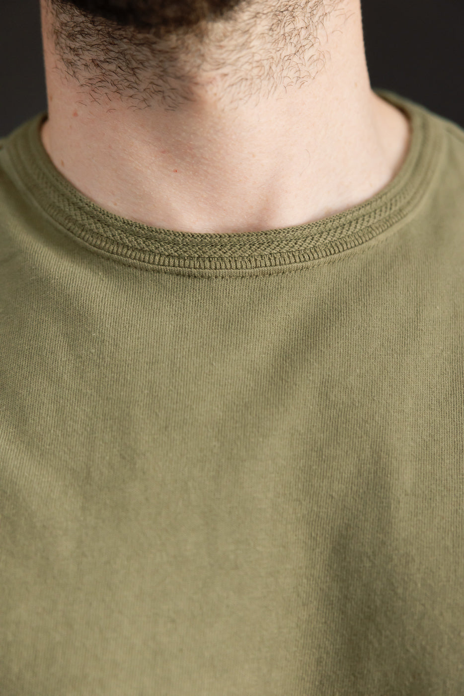 Close-up front view of olive green crew neck tee, showing ribbed collar detail on male model