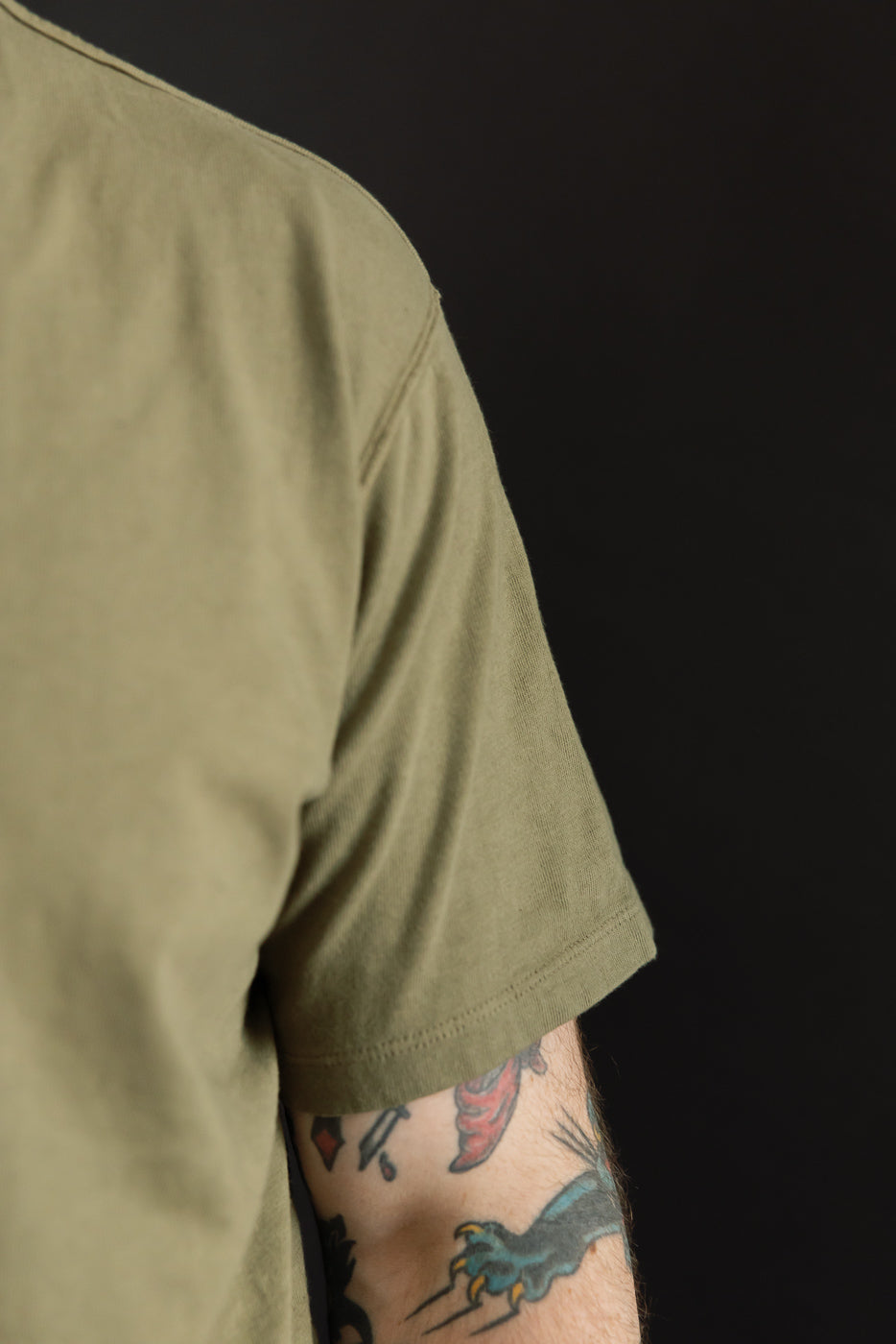 Close-up side view of male model’s olive tee, showing sleeve hem and shoulder seam, athletic build