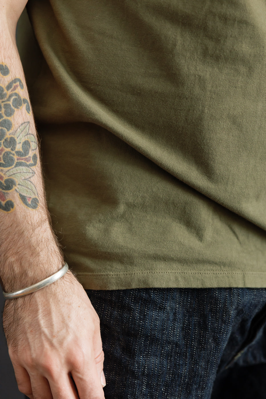 Close-up side view of olive t-shirt hem on male model, 5'9