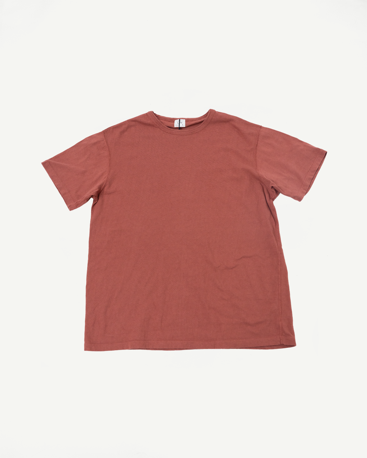 Flat lay front view of rust-colored short-sleeve crew neck tee with visible tag, showcasing fabric texture and hem detail