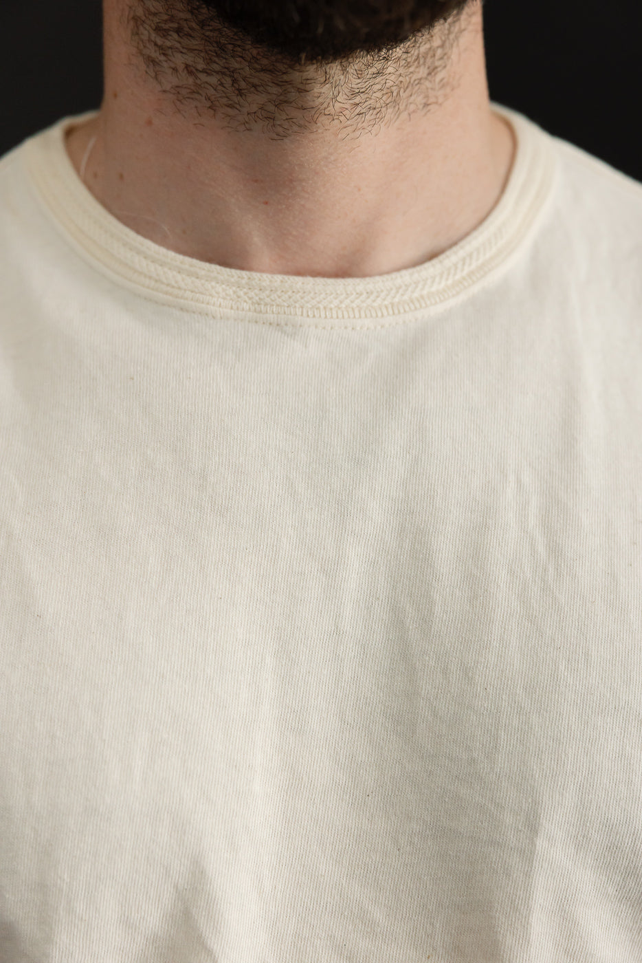 Close-up front view of male model's crew neck tee, showcasing ribbed collar and soft cotton texture