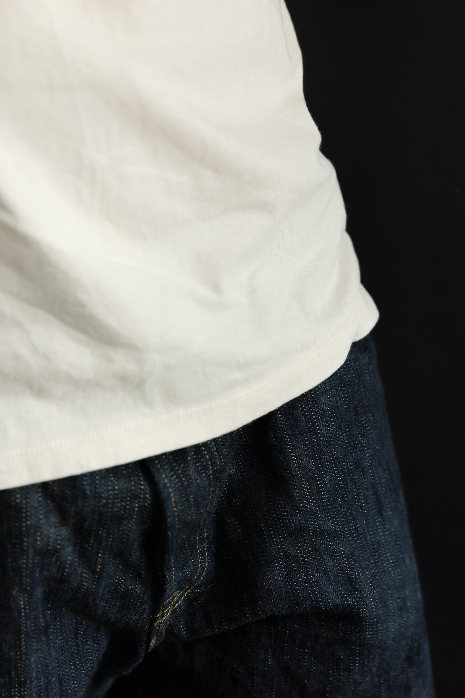Close-up side view of male model's waist, showing white tee hem and dark selvedge denim texture