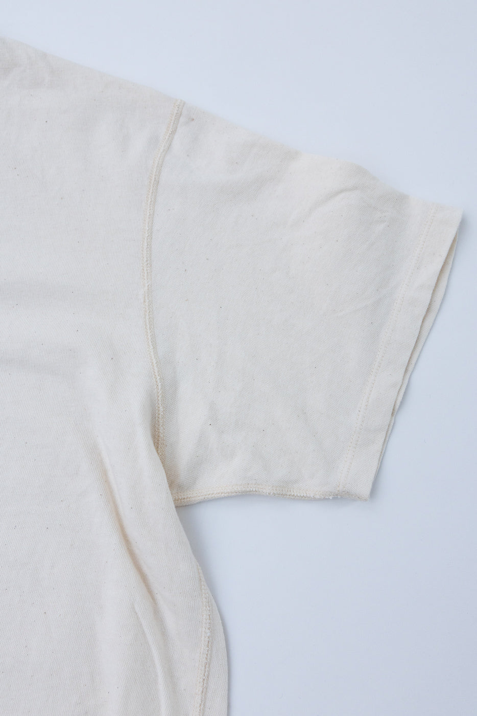 Close-up front view of off-white t-shirt sleeve showing raw hem and seam detail, natural cotton texture