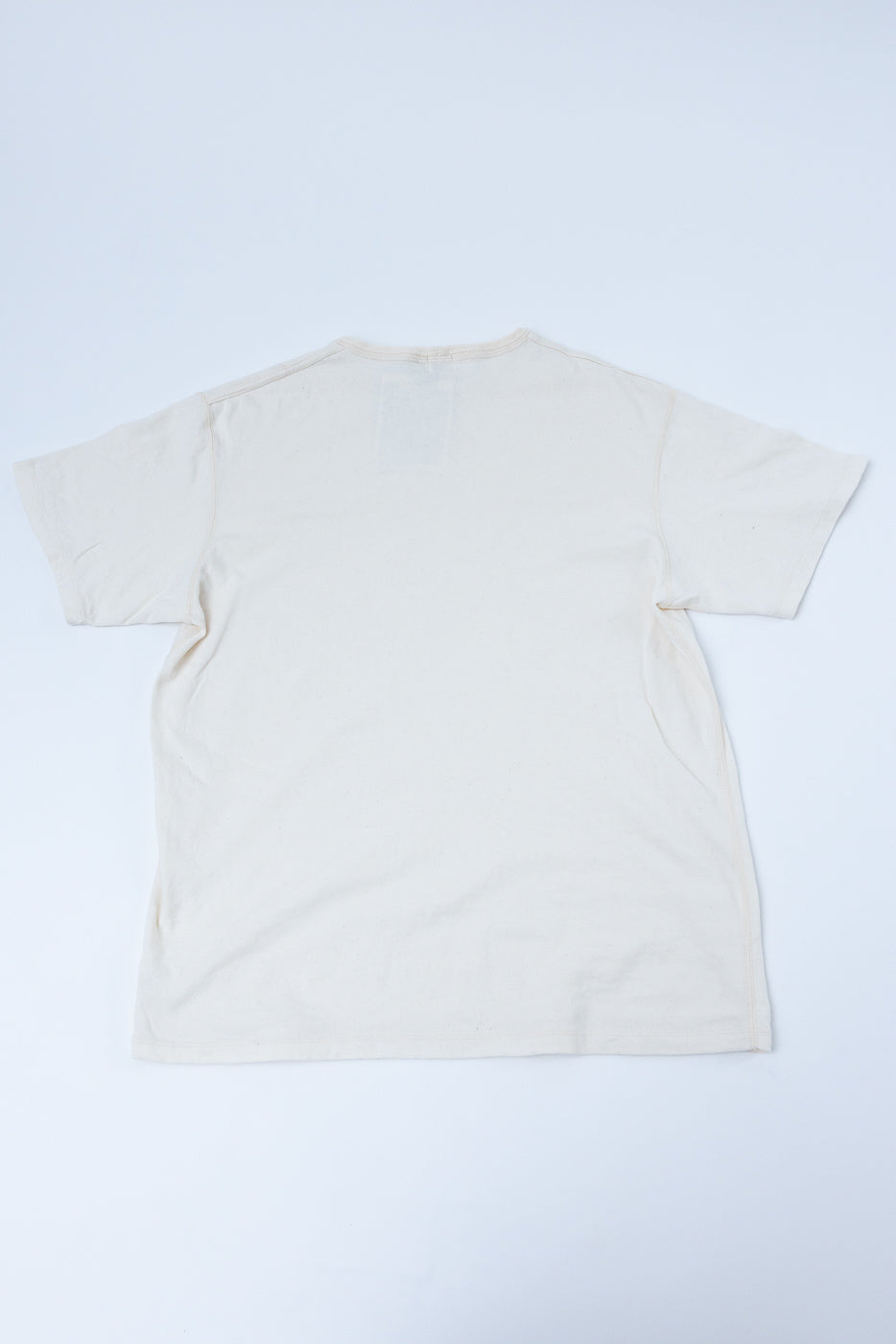 Back view flat lay of off-white crew neck t-shirt, showing tag at neckline and clean hem