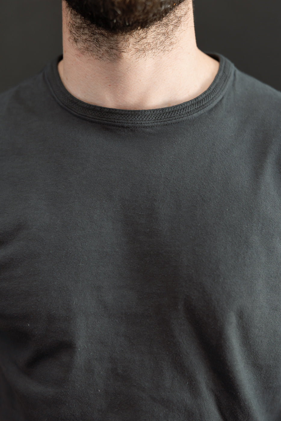 Close-up front view of a male model's neck and crew neck t-shirt, showcasing fabric texture and fit.