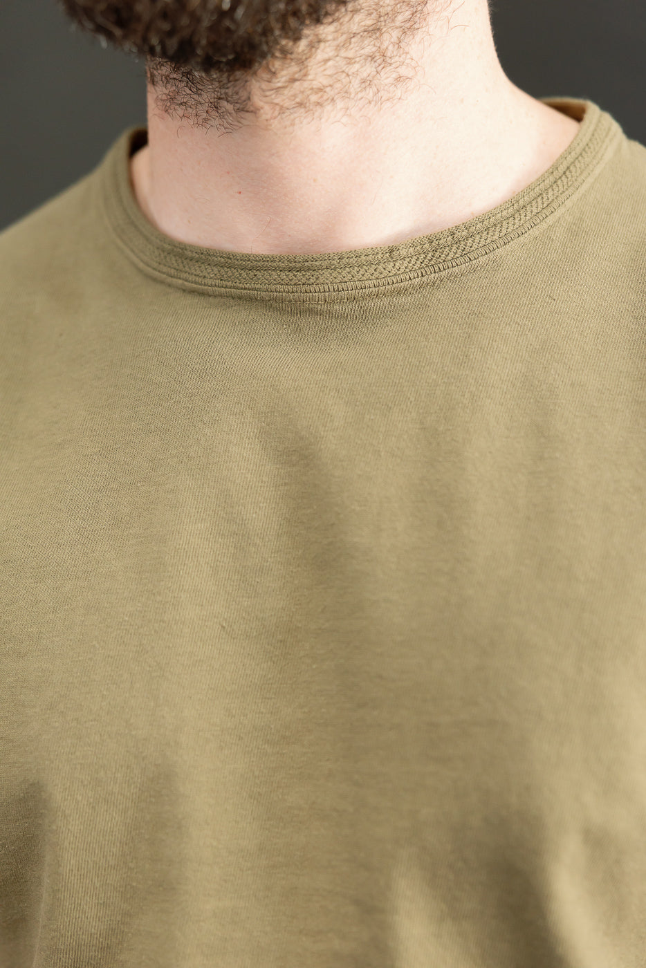 Close-up front view of olive green t-shirt collar on male model, showcasing ribbed neckline texture.