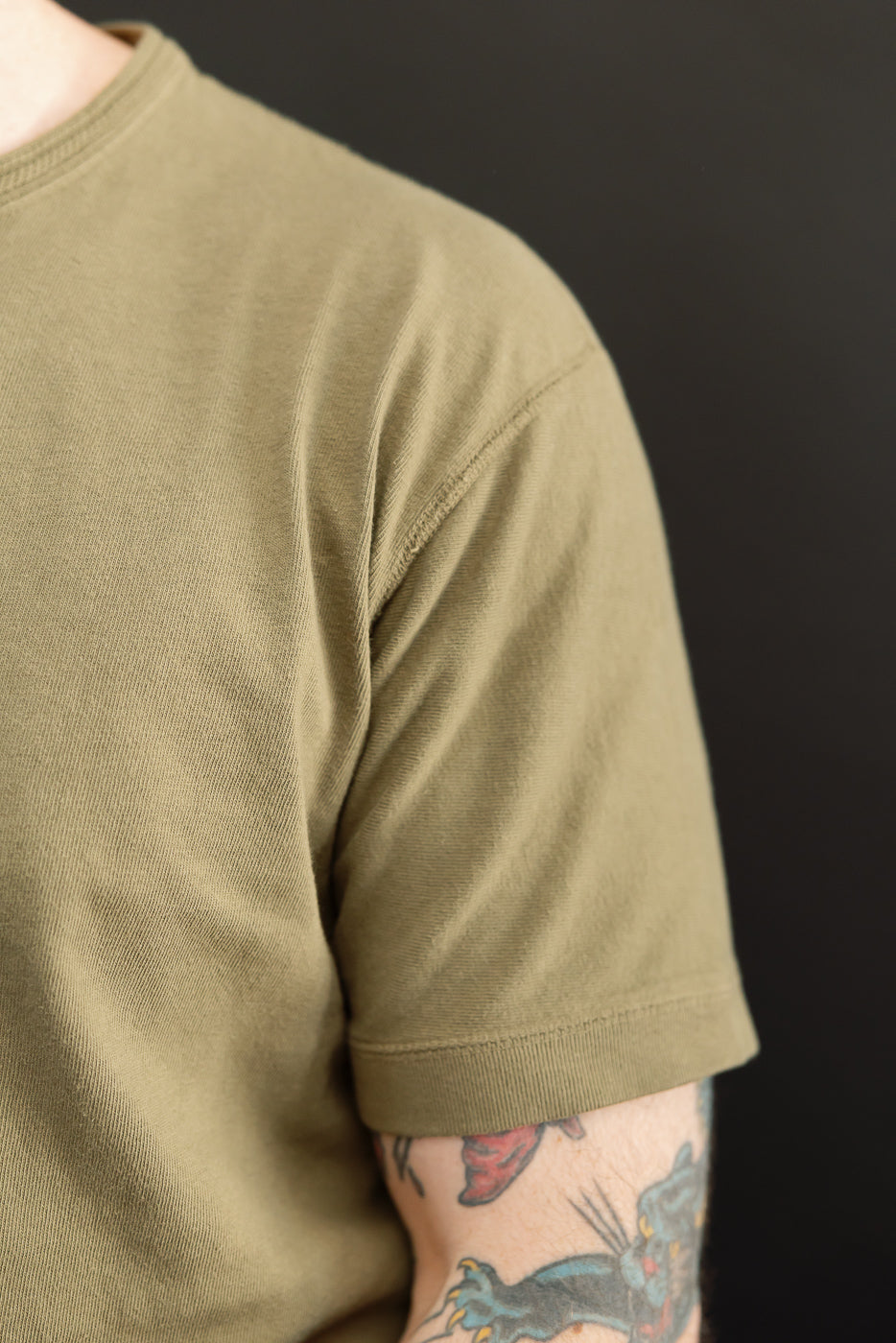 Close-up of olive green t-shirt sleeve, male model, athletic build, showing ribbed hem and fabric texture