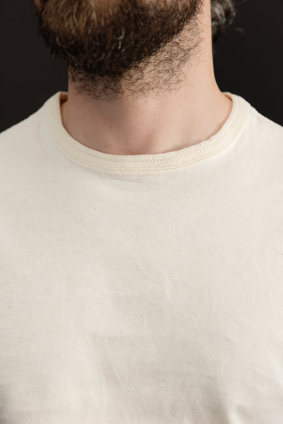 Close-up front view of cream crew neck tee, showcasing ribbed collar texture on male model.