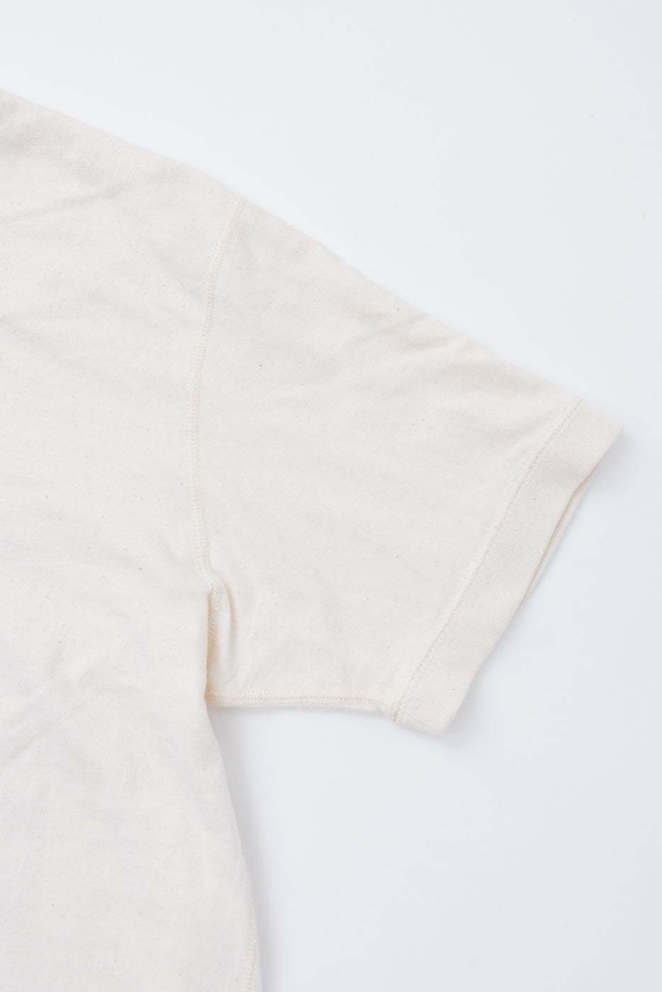 Close-up of cream t-shirt sleeve, showing ribbed hem and fabric texture, front view