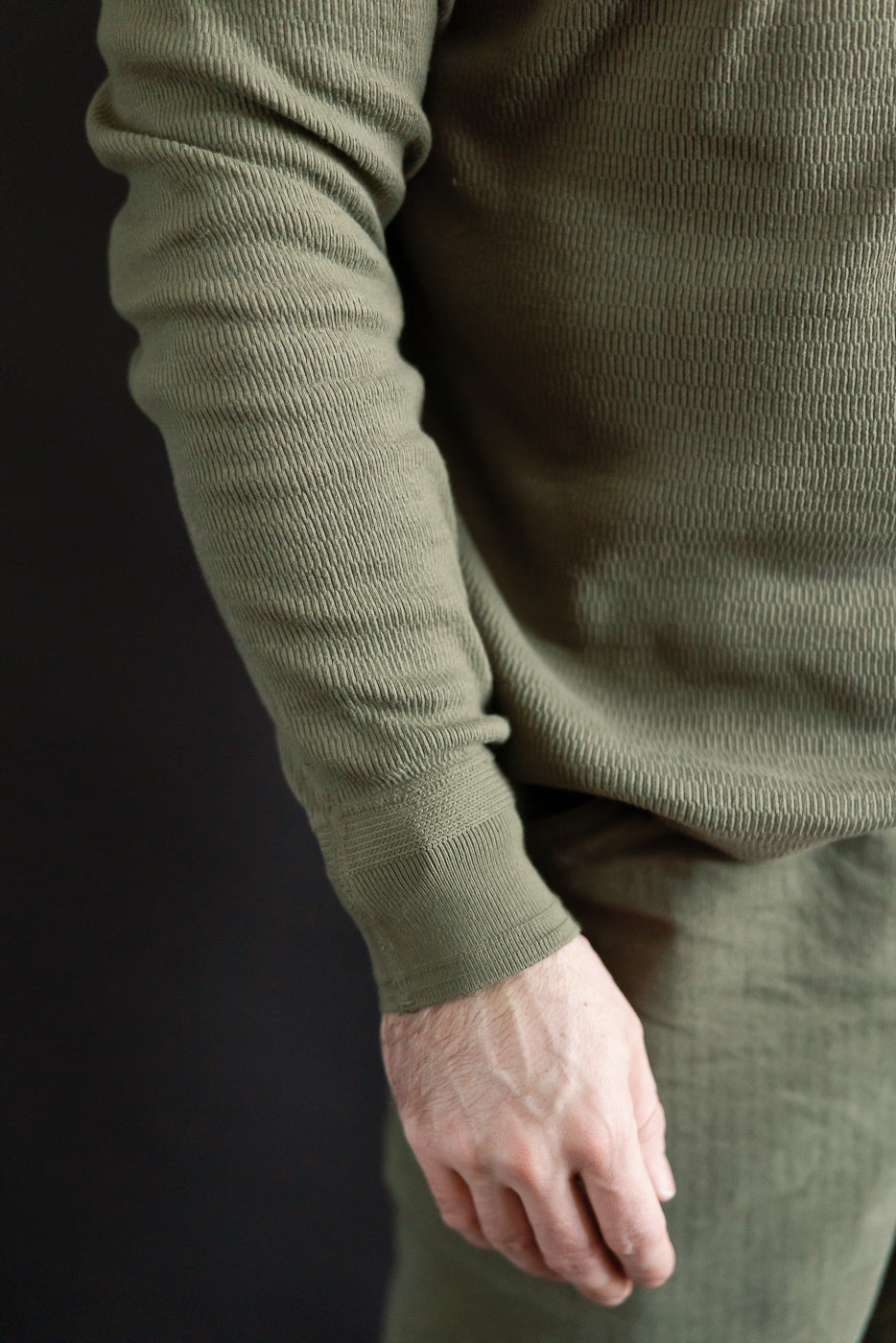 Close-up of male model's right side wearing Loop & Weft Supima honeycomb knit thermal in army olive, showing fabric texture and ribbed cuff. Model is 5'9
