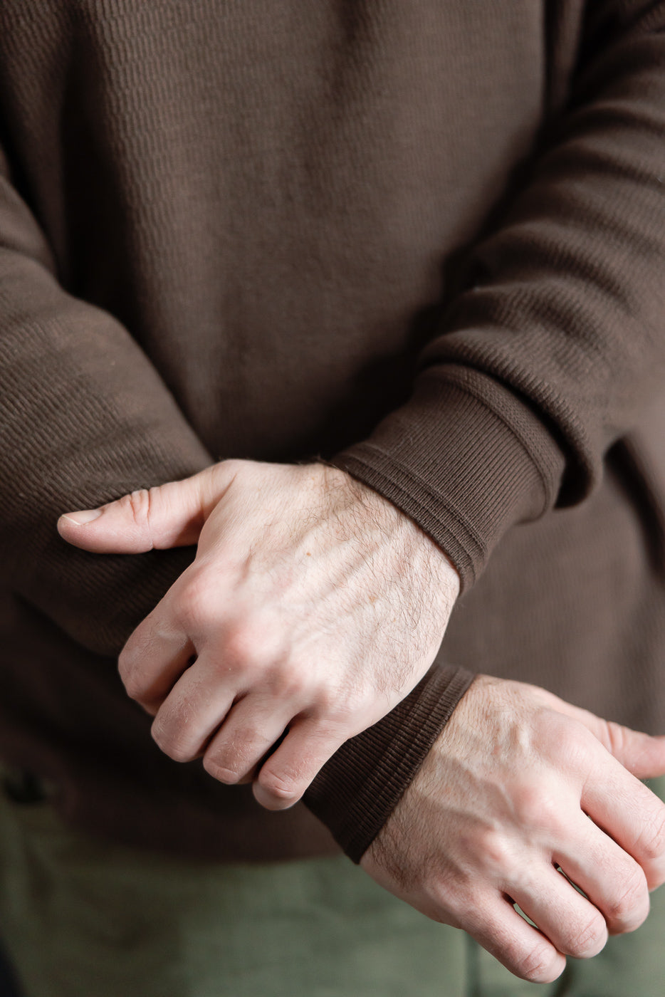 Close-up of male model's hands and ribbed cuffs on brown Supima honeycomb knit thermal, front view.