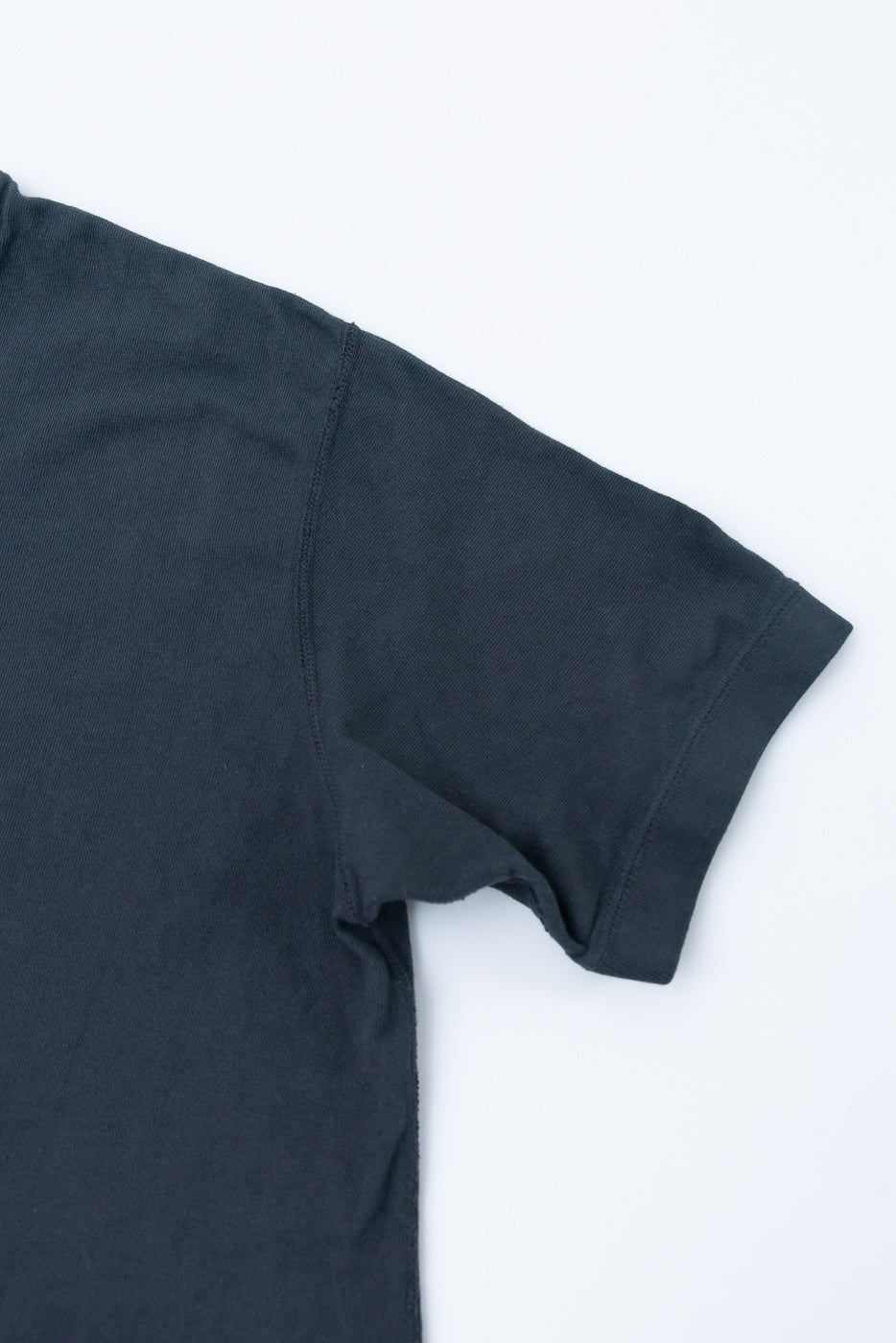 Close-up of dark gray t-shirt sleeve and shoulder, showcasing ribbed texture and stitching detail