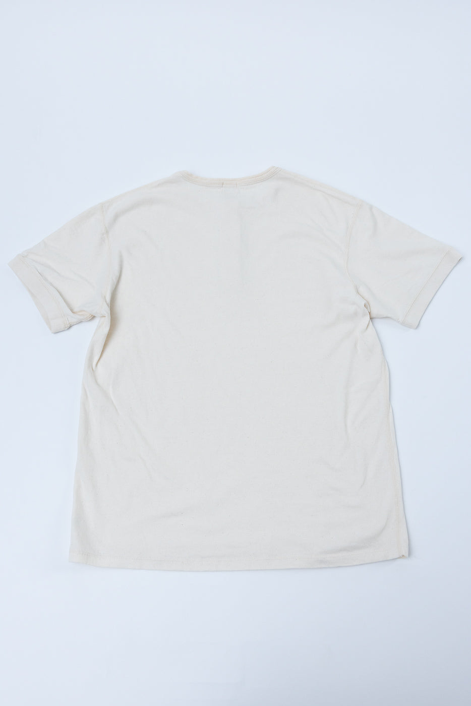 Back view of cream-colored casual t-shirt, flat lay, showcasing hem and sleeve details
