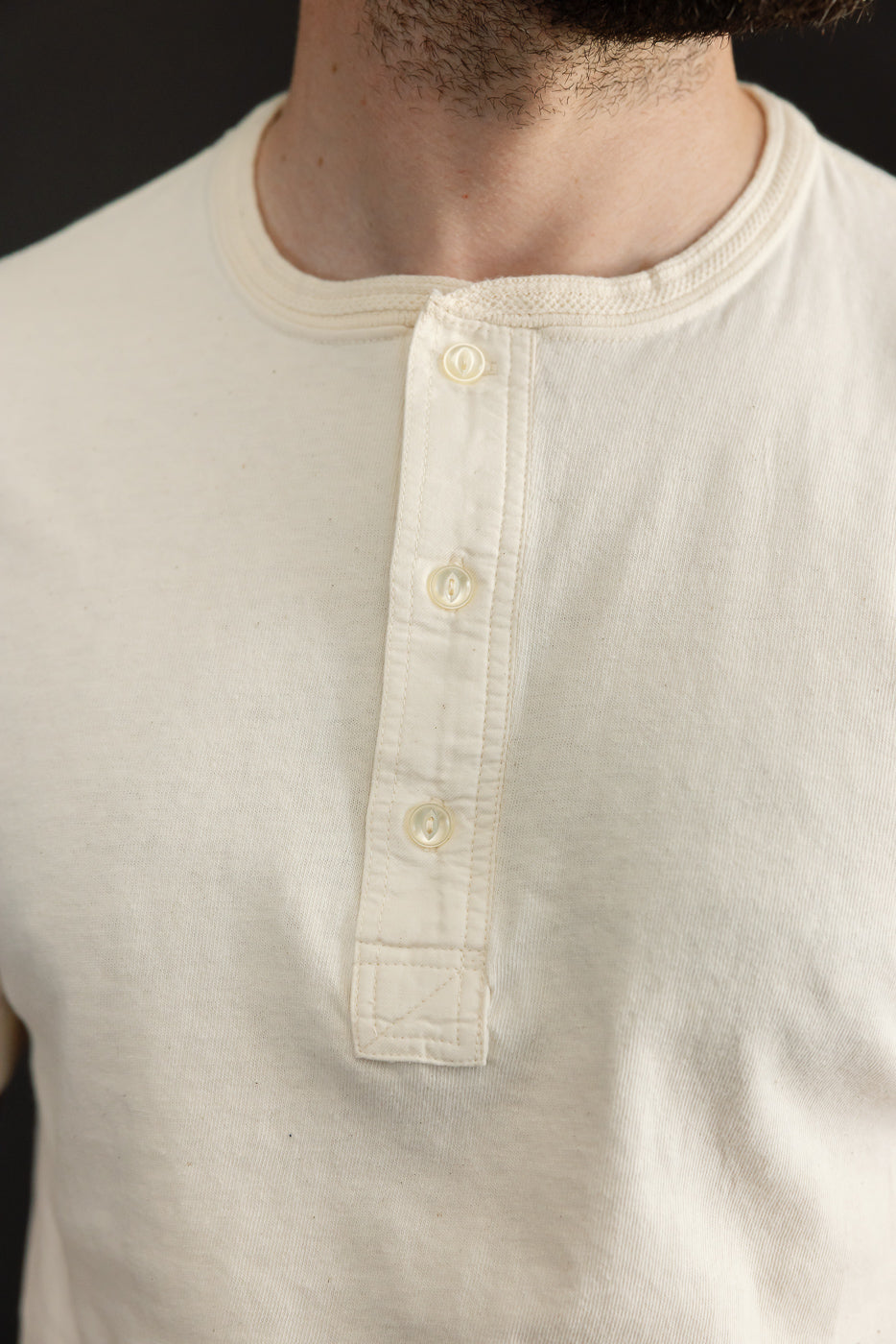 Close-up front view of male model's cream henley shirt with button placket and ribbed collar