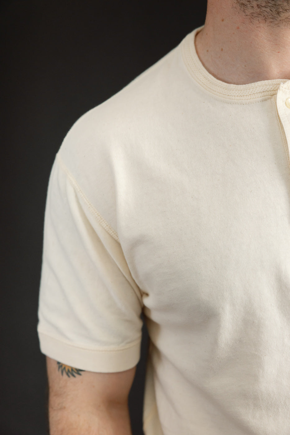 Close-up of male model's shoulder and sleeve, showcasing cream henley with ribbed collar and hem.