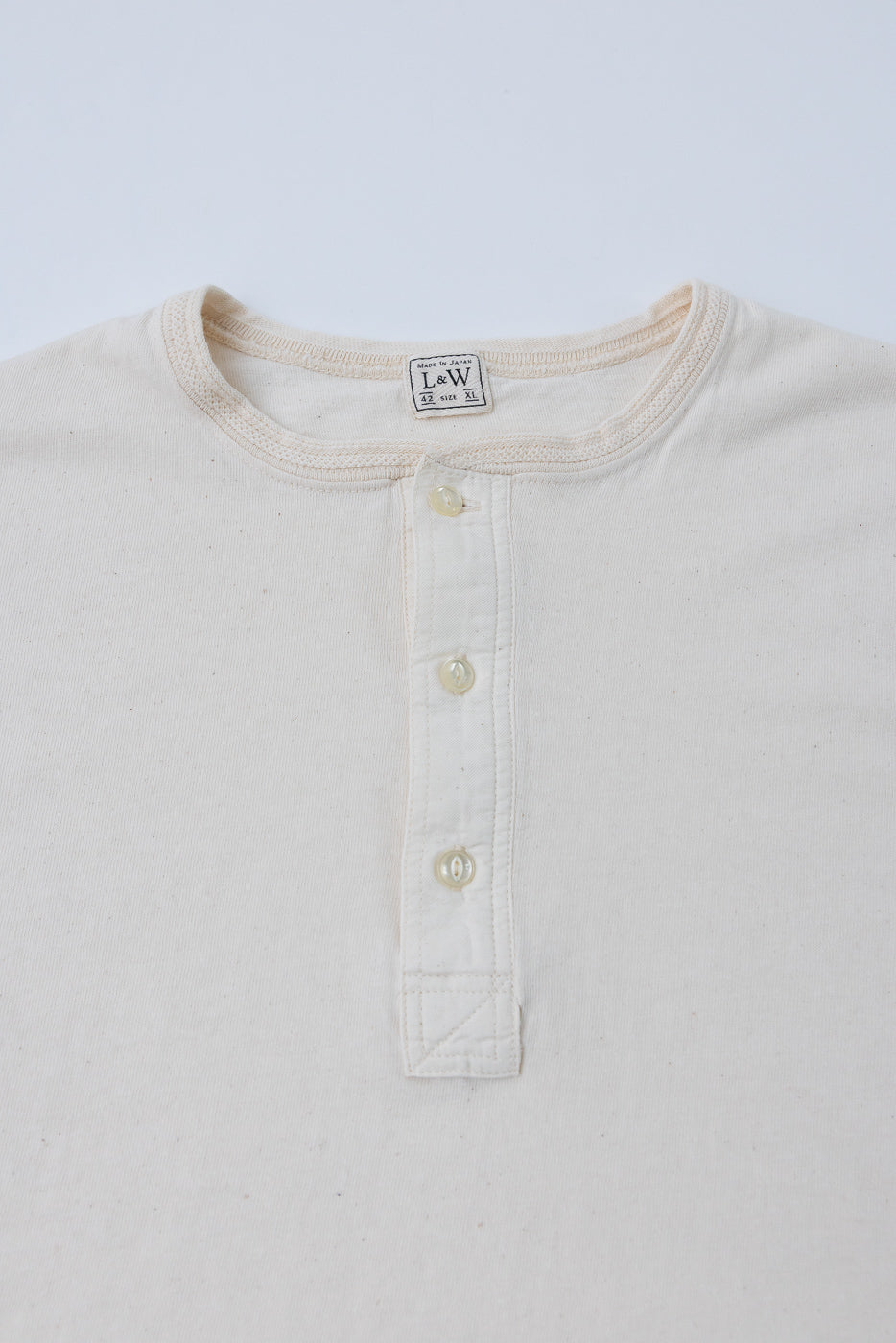 Close-up front of cream henley shirt showing L&W tag, buttons, and ribbed collar, made in Japan