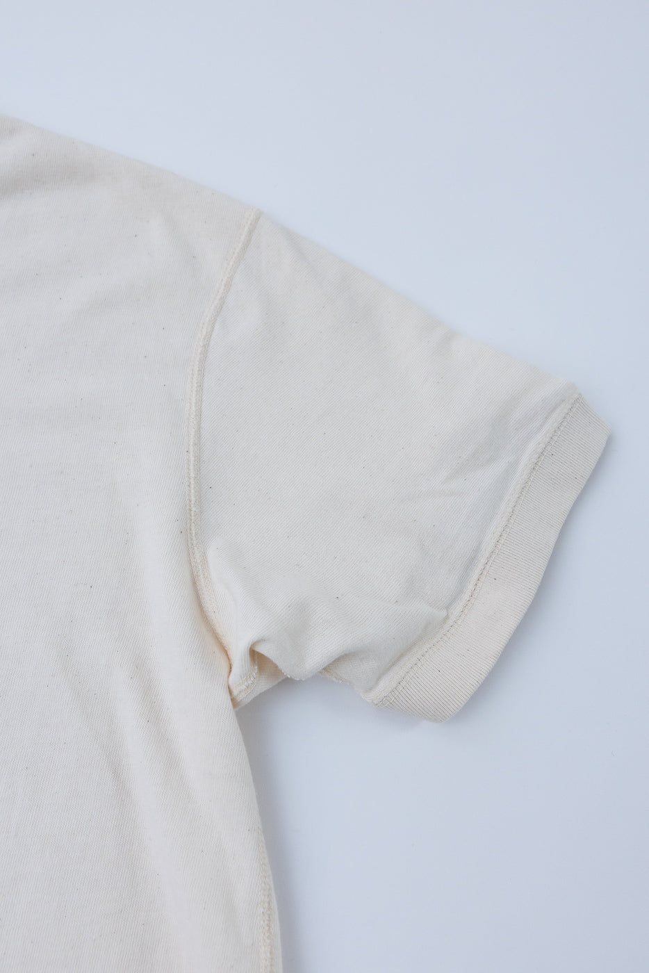 Close-up front view of cream cotton tee sleeve, ribbed cuff, shoulder seam detail, soft texture