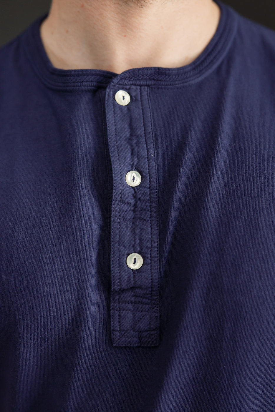 Close-up front view of navy henley shirt with white buttons, worn by male model, 5'9
