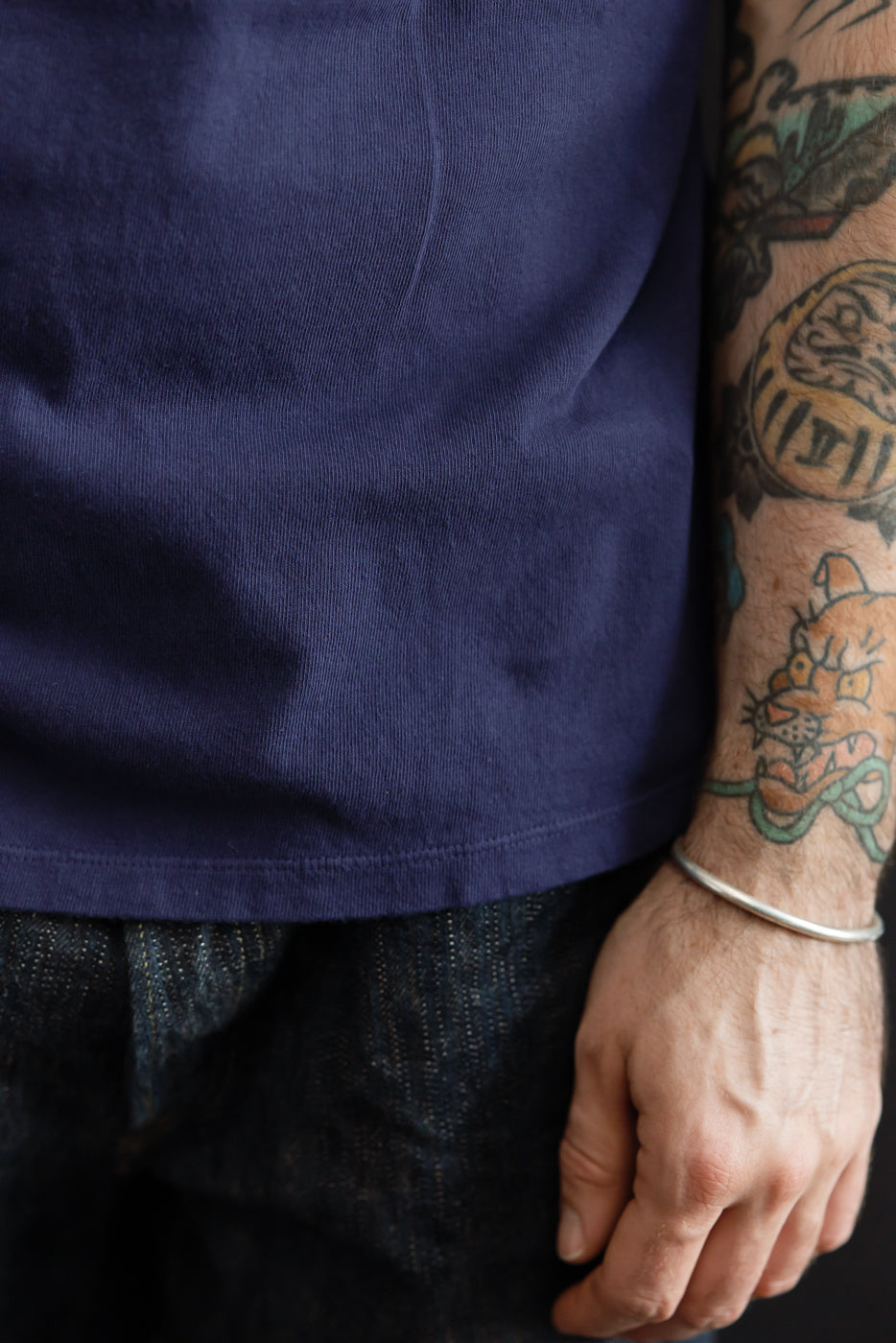 Close-up of navy t-shirt hem, male model, athletic build, tattoos visible on arm