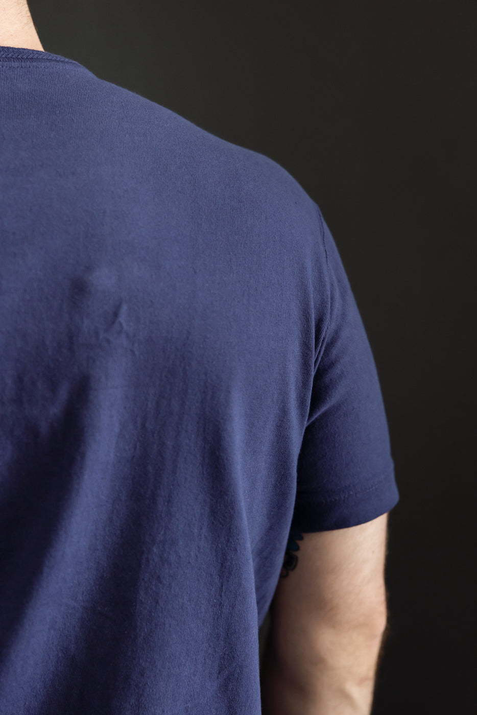 Close-up back view of navy t-shirt on male model, showcasing fabric texture and sleeve hem