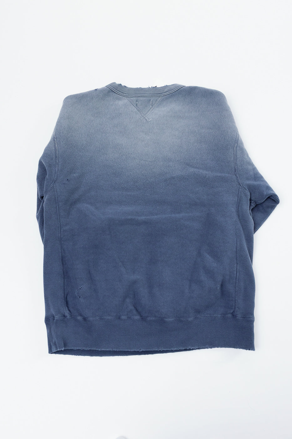 Flat lay of the back of a blue gradient ombré sweatshirt with a ribbed hem.