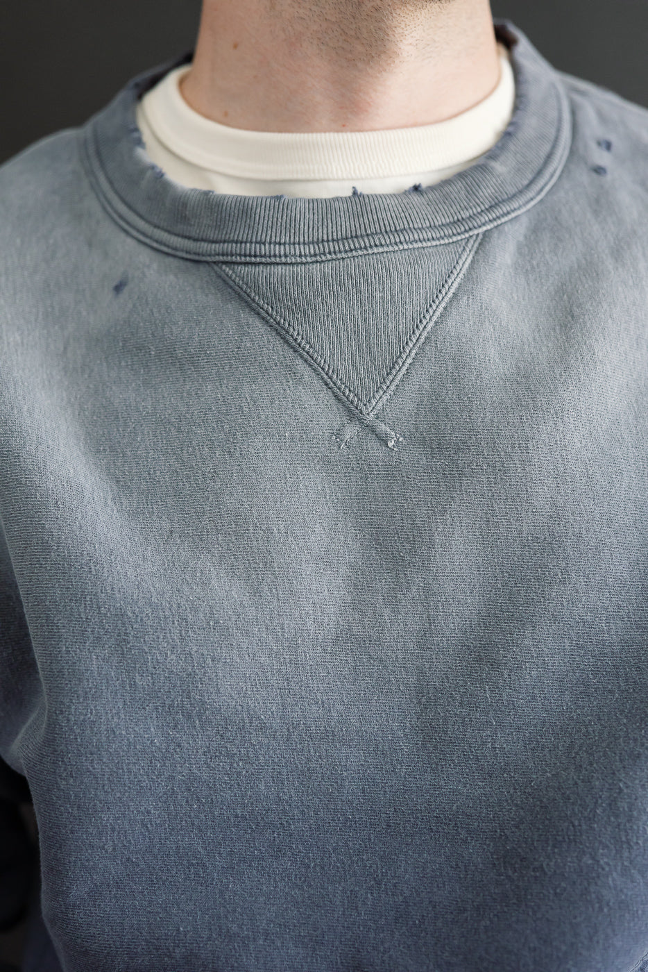 Close-up of the front neckline of a grey sweatshirt on a male model, 5'9