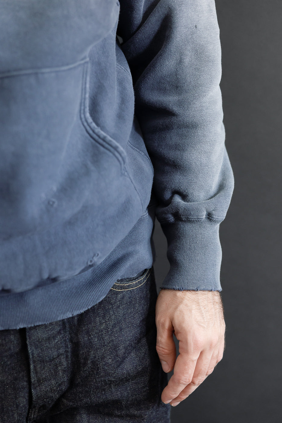 Close-up side view of a blue washed hoodie sleeve and ribbed cuff on a 5'9