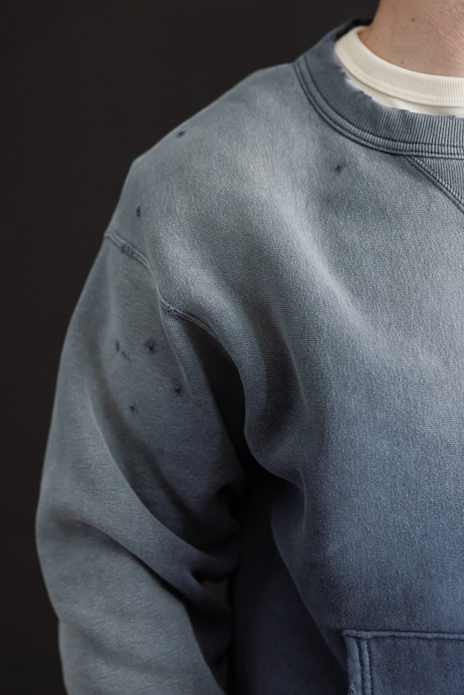 Close-up of the left sleeve and shoulder of a blue crewneck sweatshirt showing fabric texture.