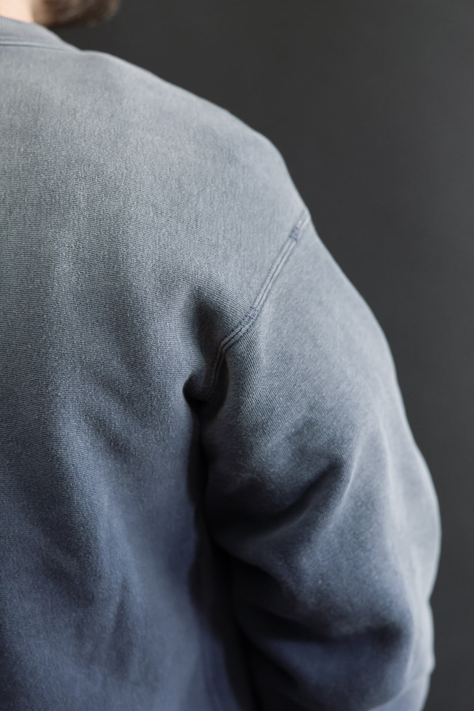 Close-up of the back and shoulder of a grey sweatshirt showing fabric texture.