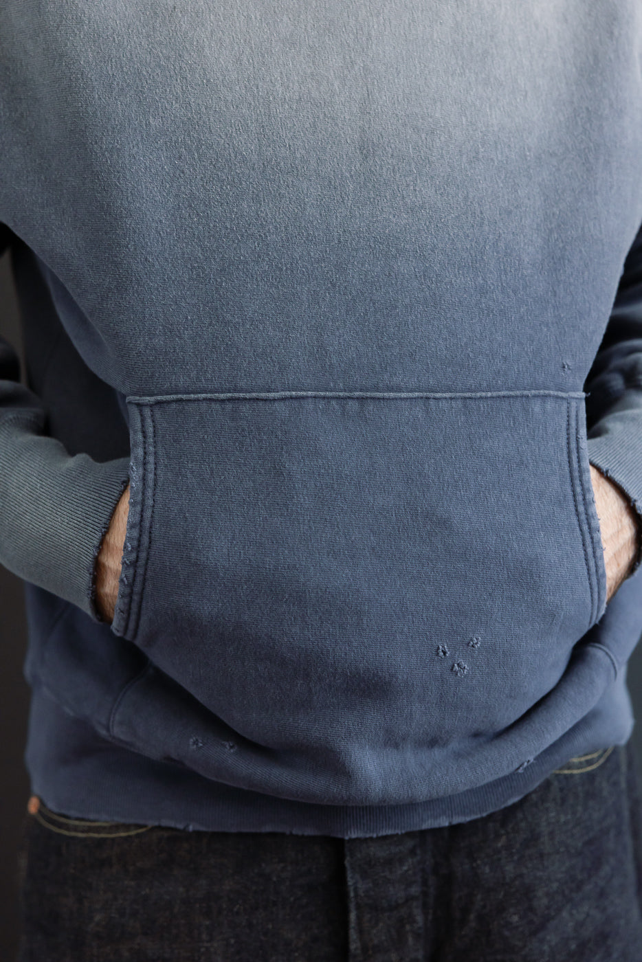 Close-up front view of a blue washed hoodie pocket detail on a male model.