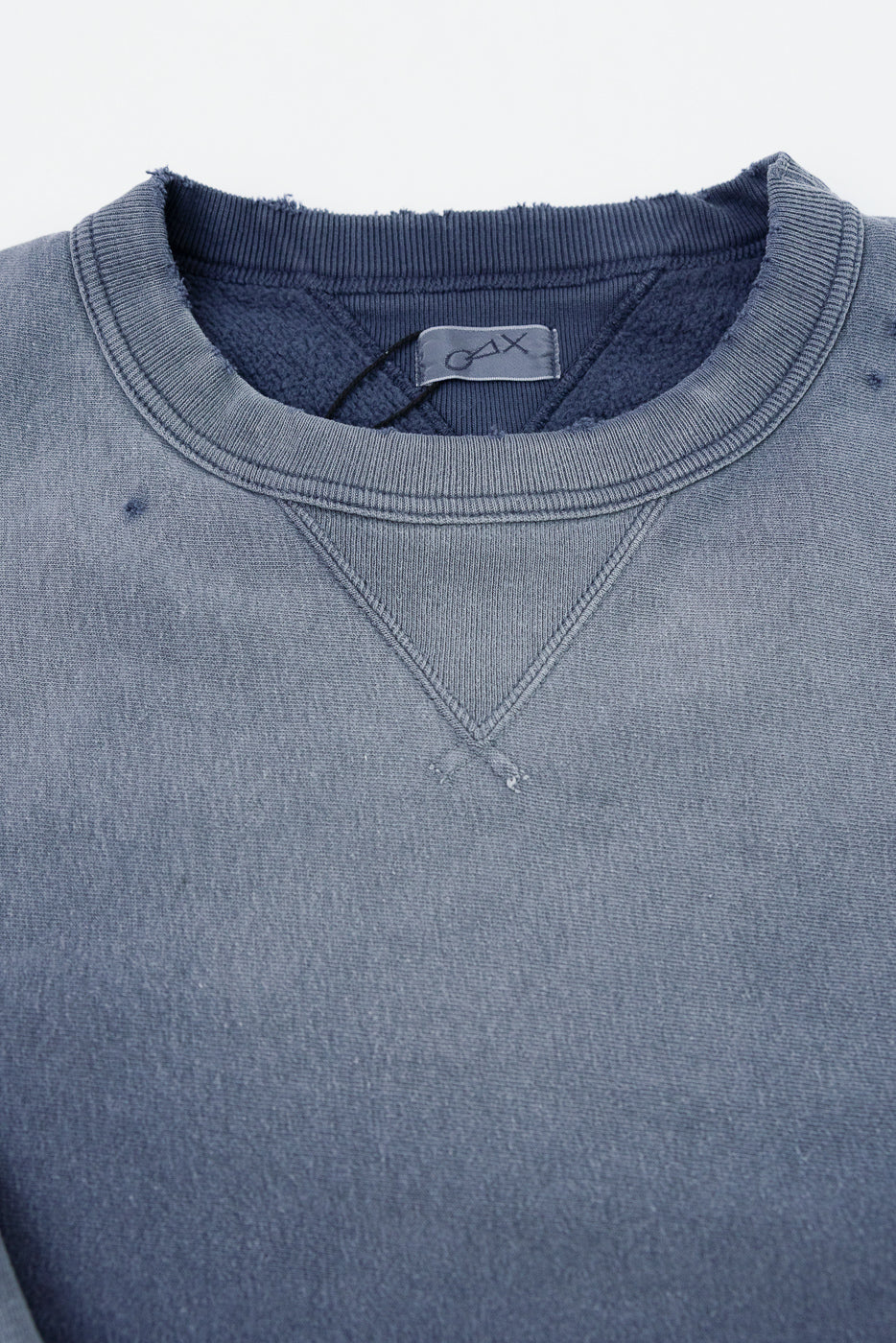 Close-up of the front neckline of a grey crewneck sweatshirt showing fabric texture and tag.
