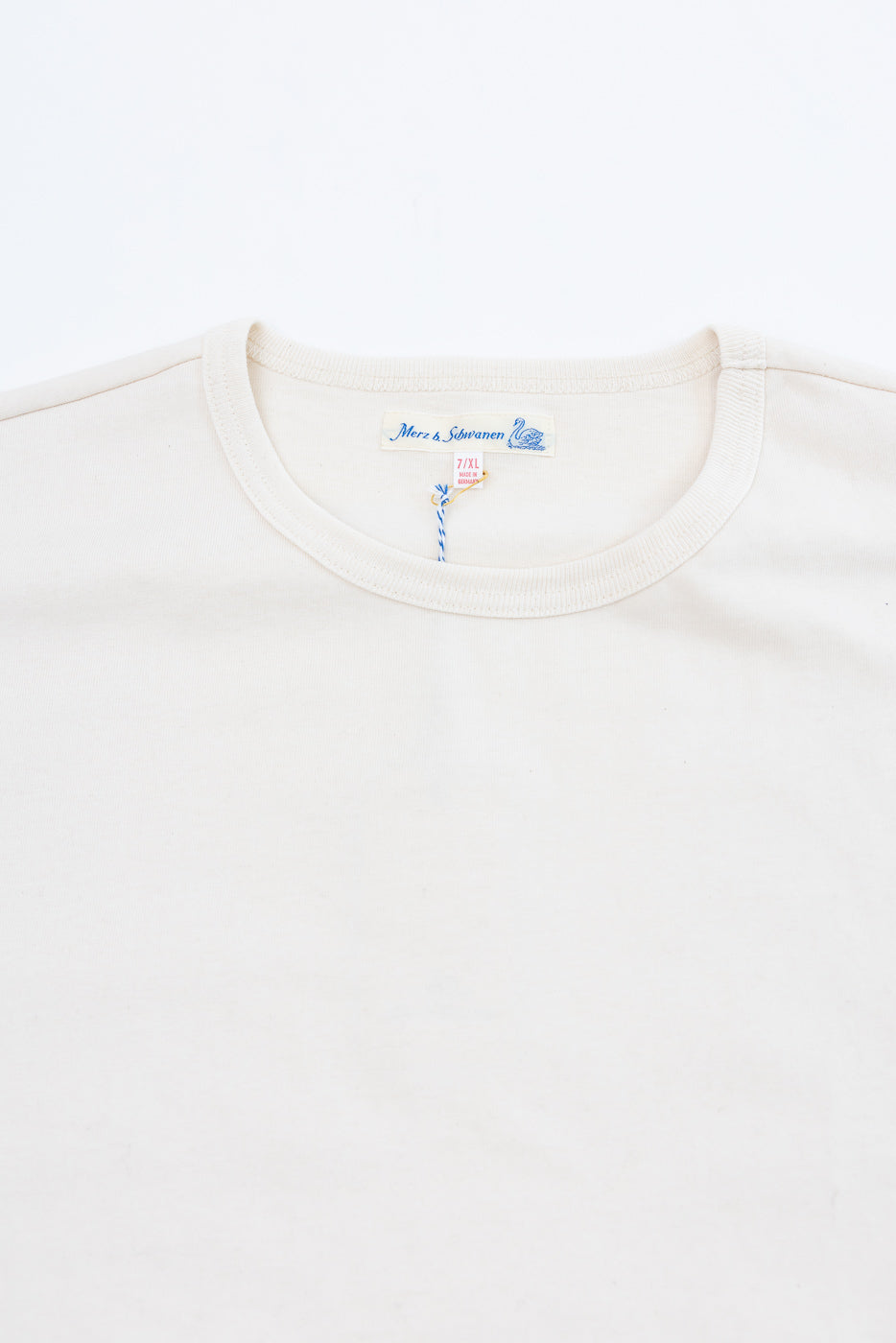 Close-up of the front neckline and Merz & Siwanen tag of a cream crewneck t-shirt.