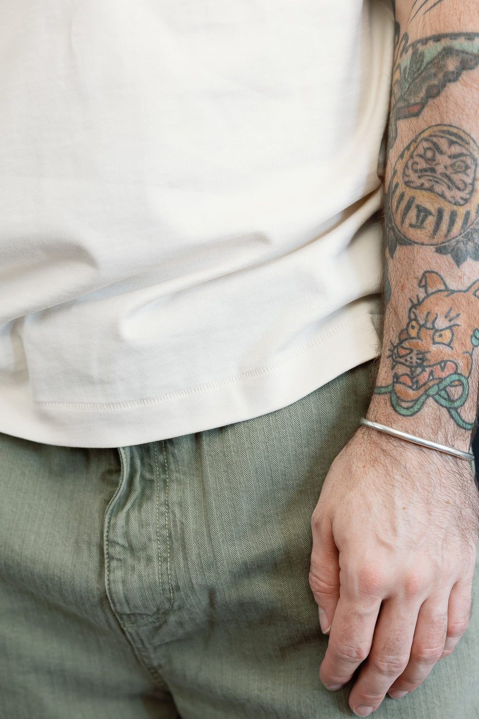 Close-up of the front hem of a white t-shirt and the waist of olive green trousers on a male model.