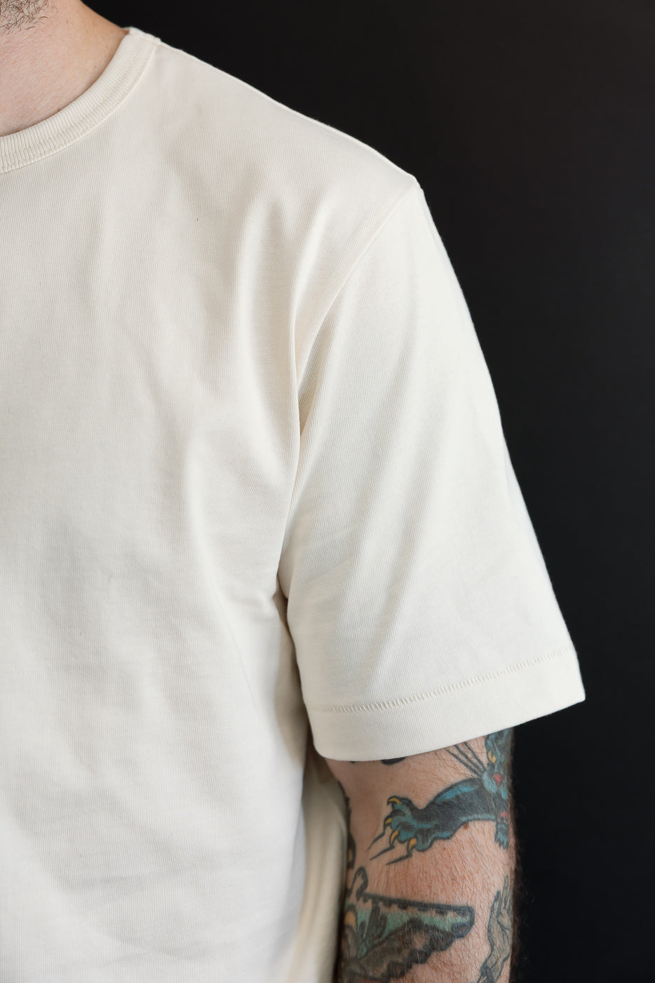 Close-up of the left sleeve and shoulder of a cream cotton t-shirt on a male model.