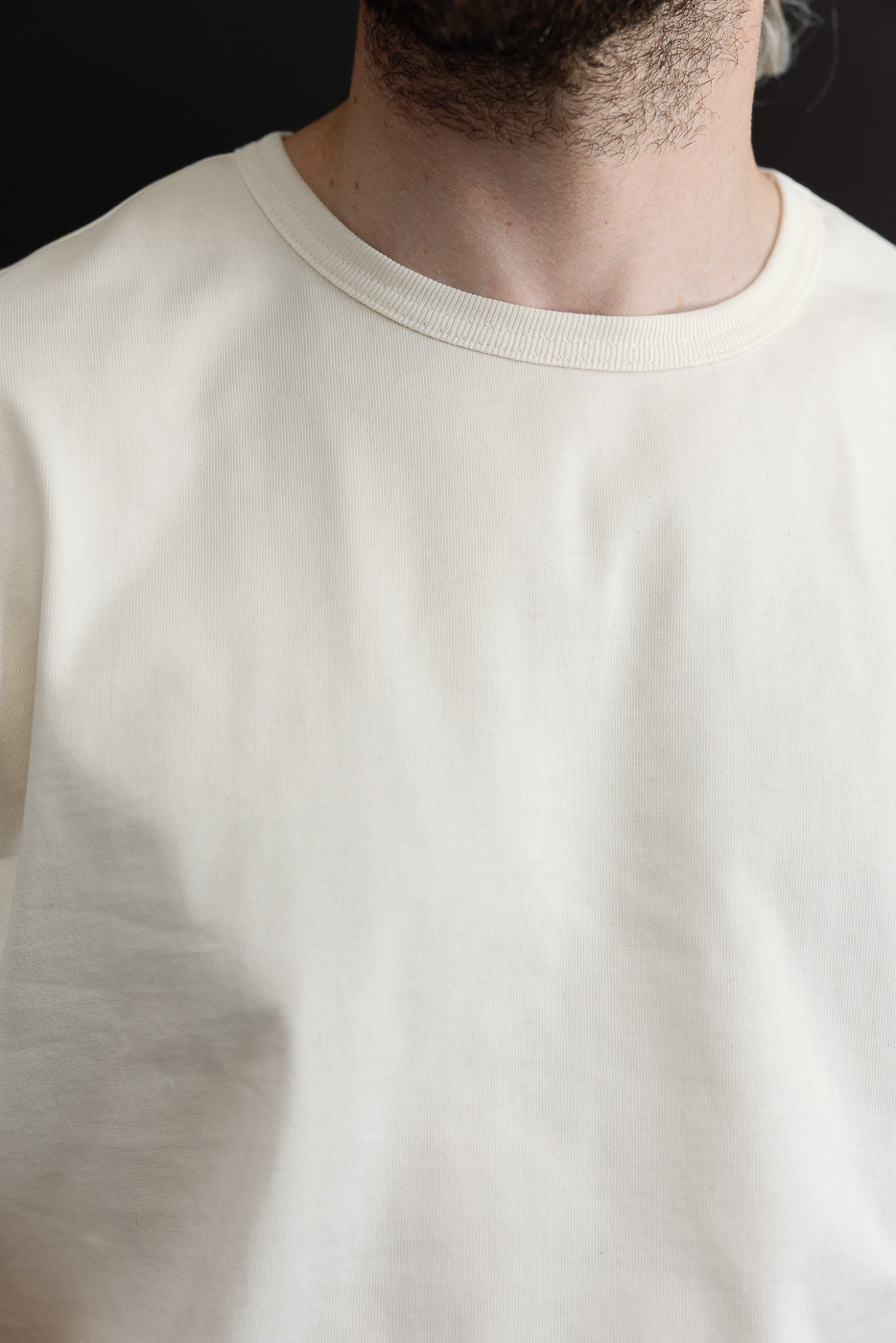 Close-up of the front neckline and crew collar of a white cotton t-shirt worn by a male model.
