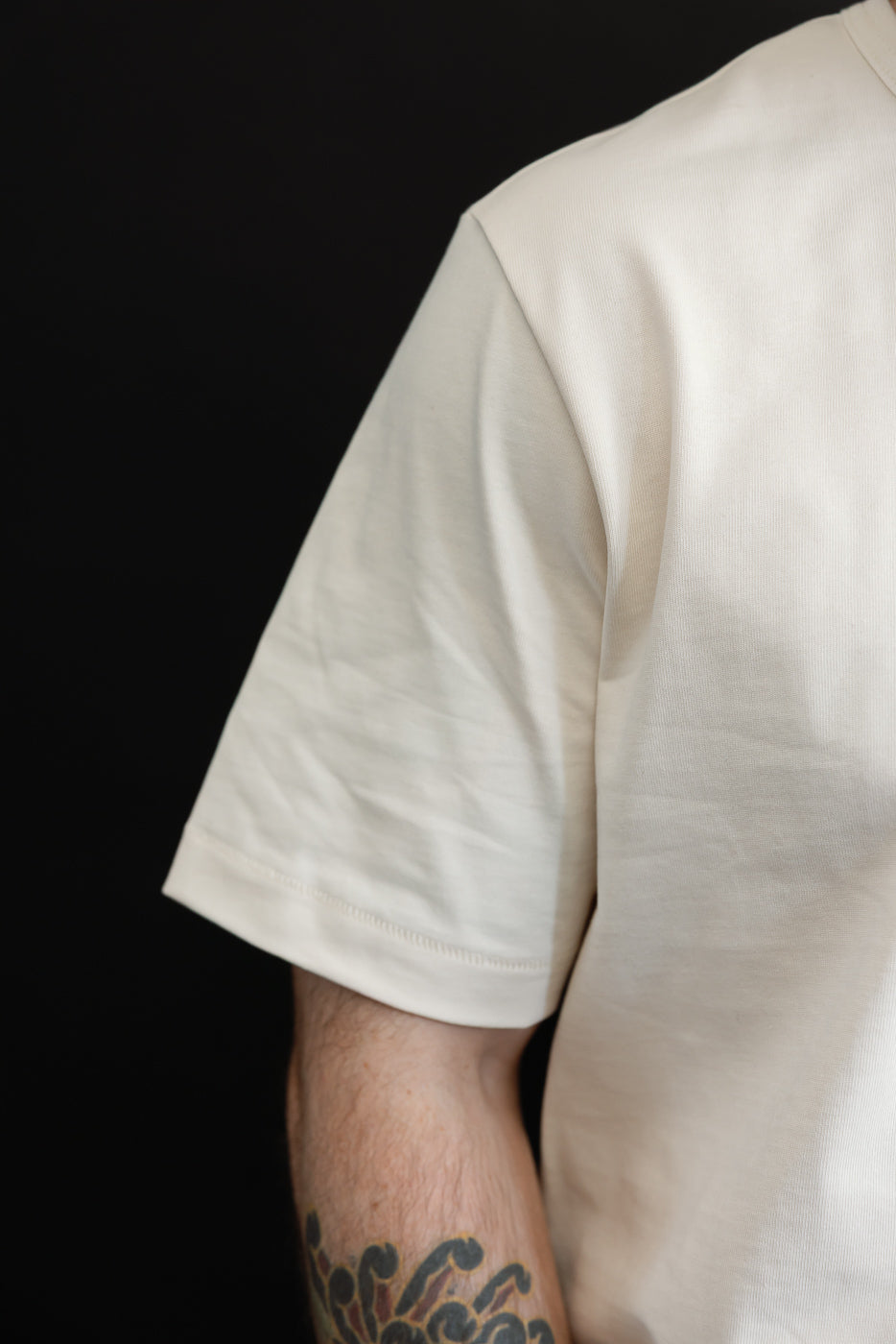 Close-up of the left sleeve and shoulder of a cream-colored t-shirt on a male model.