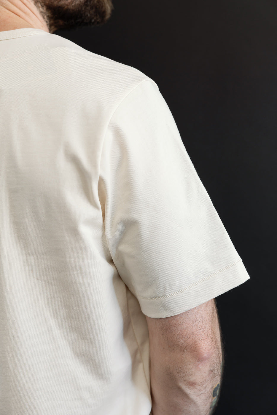 Close-up side view of the sleeve and shoulder of a cream cotton t-shirt on a male model.