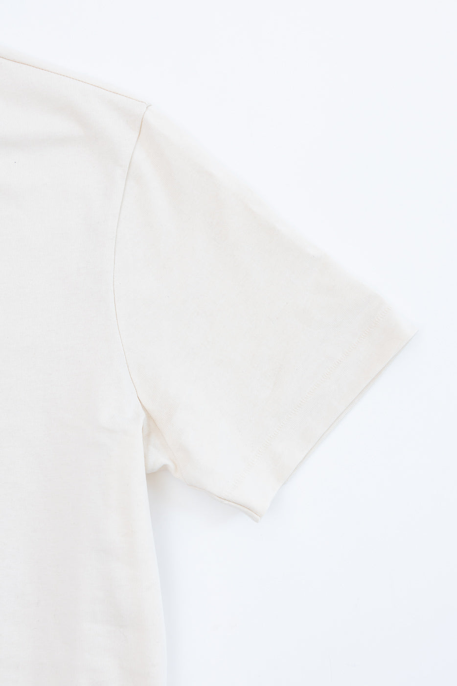 Close-up of the right sleeve and shoulder detail of a cream-colored cotton t-shirt.