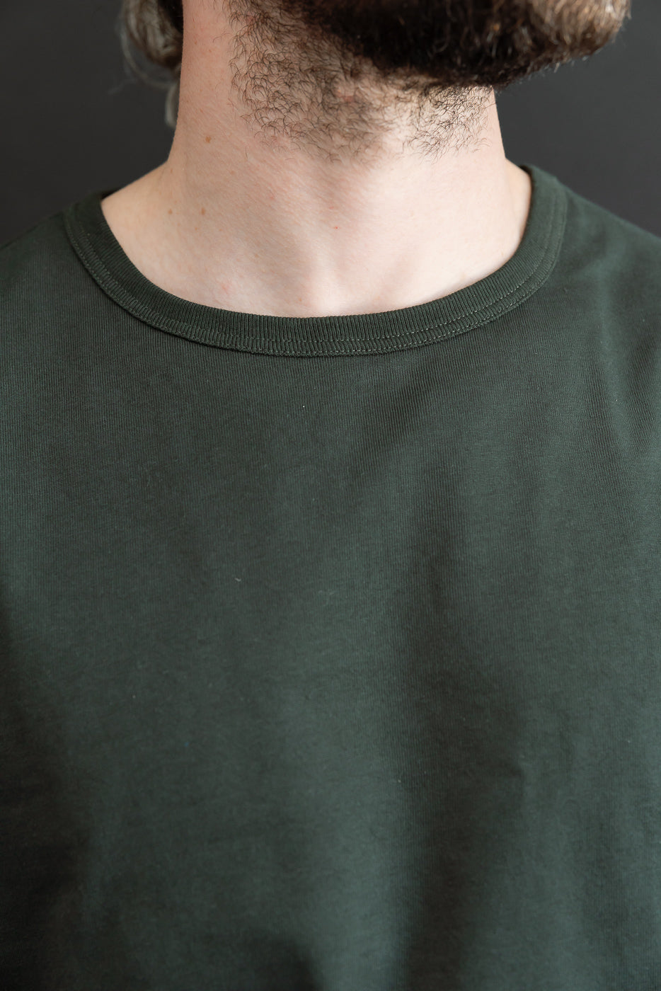 Close-up front view of the crew neck collar and olive green fabric texture on a male model.