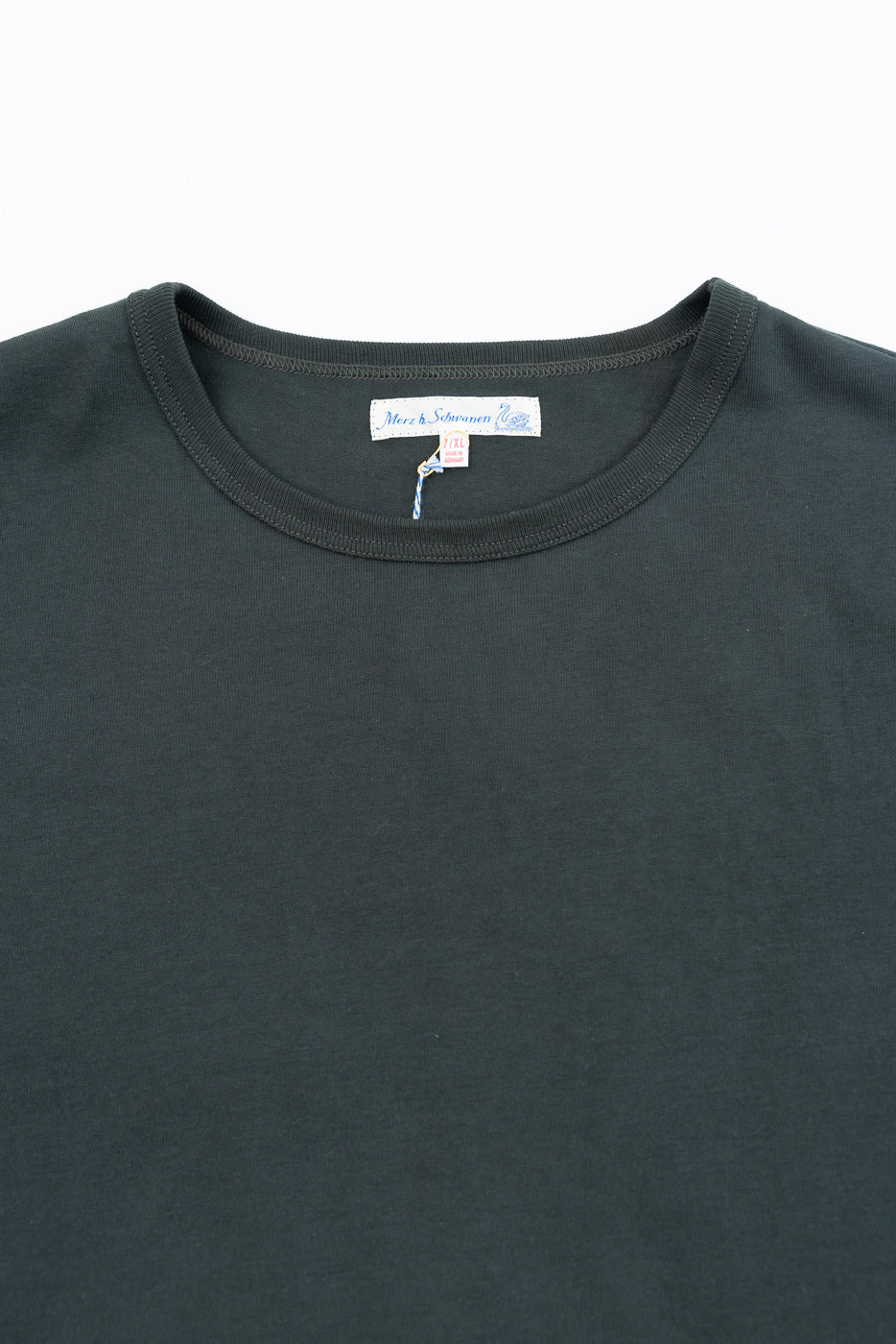 Close-up front view of the crew neck collar and Merz b. Schwannen tag on a dark grey t-shirt.