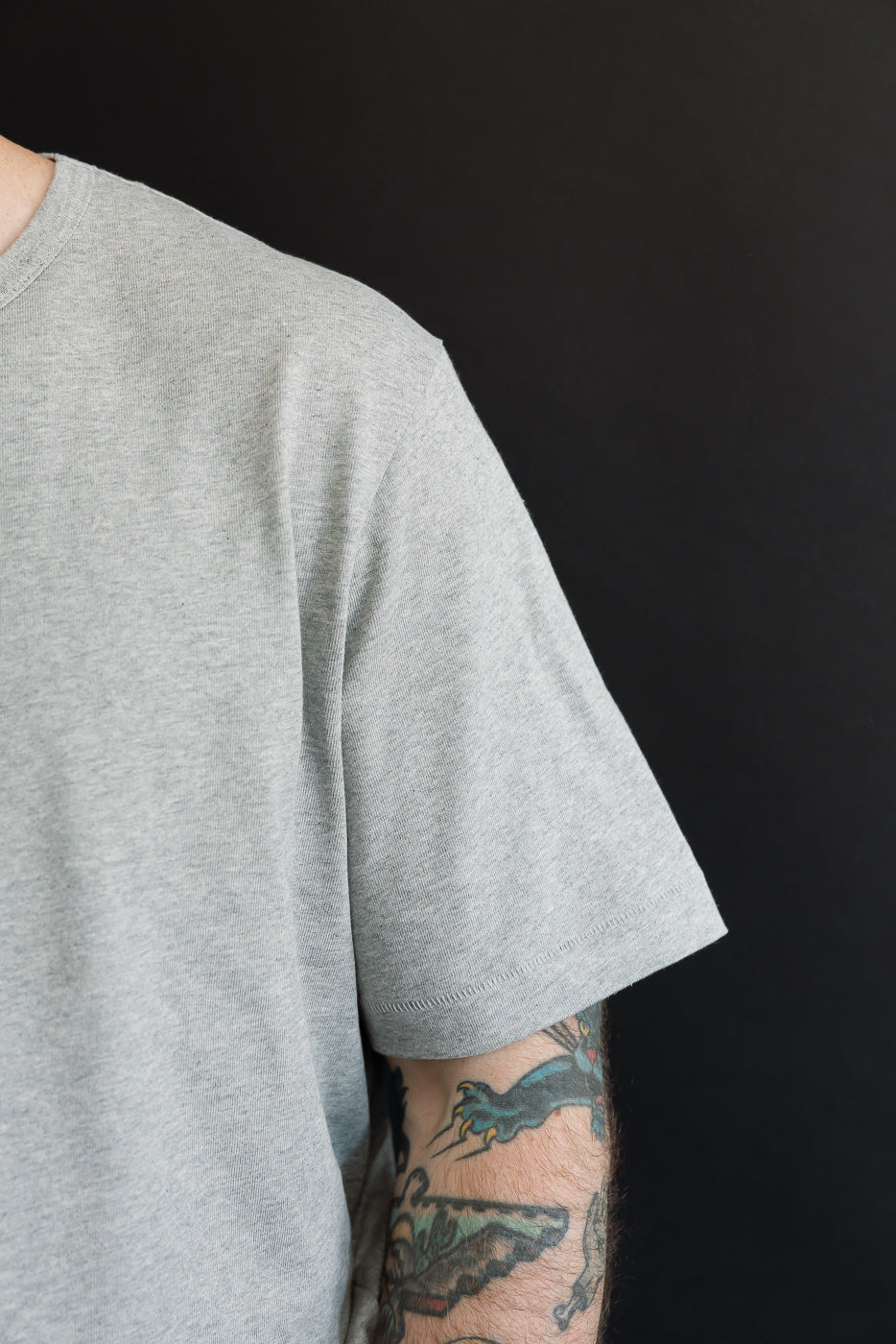 Close-up of the left sleeve and shoulder of a grey cotton t-shirt on a male model.