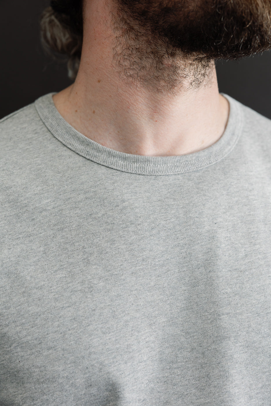 Close-up front view of the crew neckline and heather grey fabric texture on a male model.