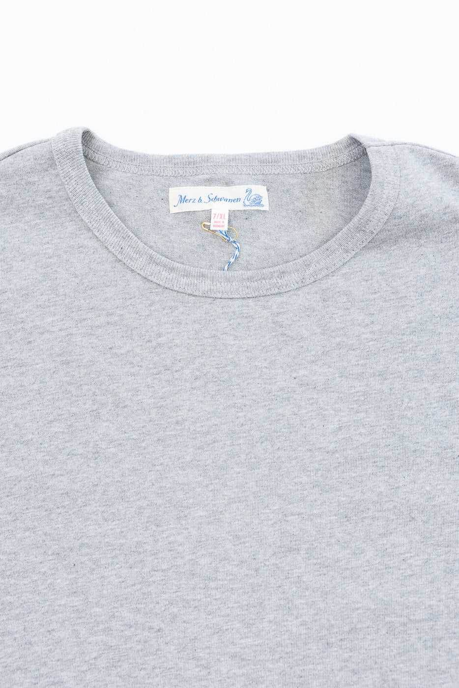 Close-up of the front neckline of a grey t-shirt showing the Merz b. Schwanen size tag.