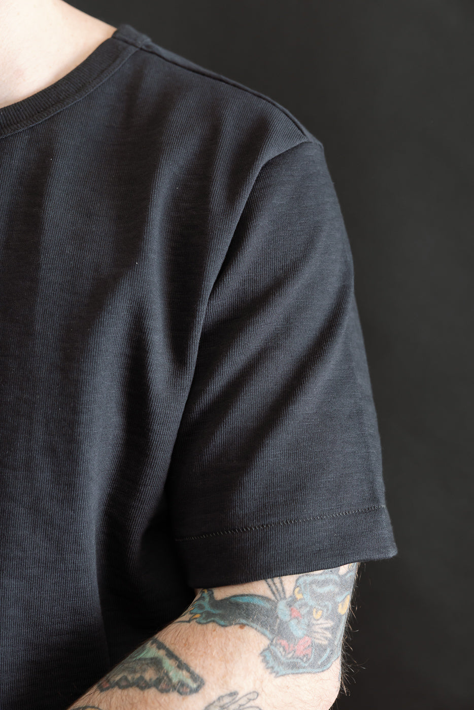 Close-up of male model’s right shoulder in charcoal heavy loopwheeled t-shirt, sleeve and fabric texture shown.