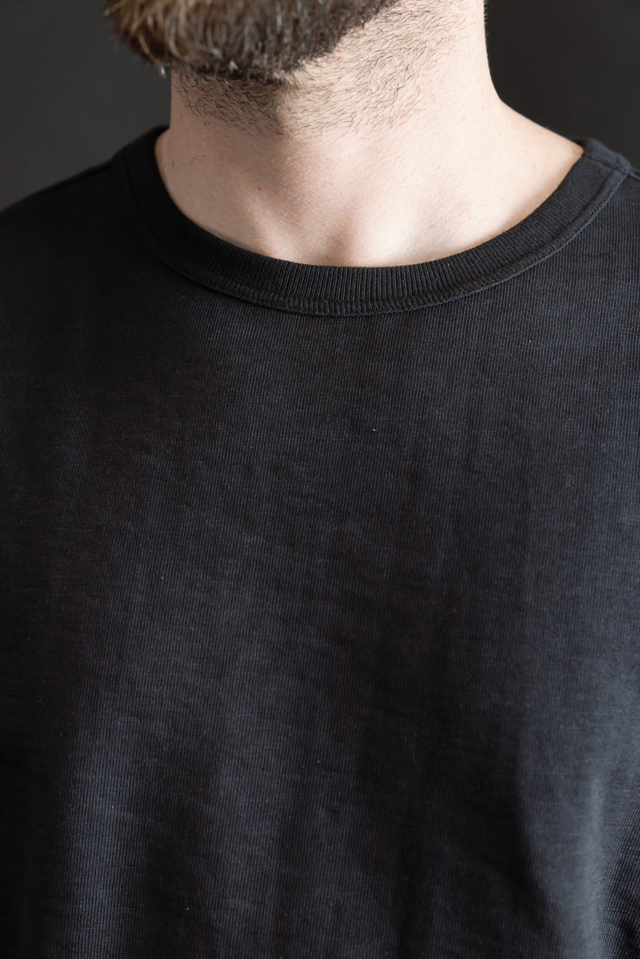 Close-up of male model, 5'9”, 165lbs, athletic build, wearing charcoal loopwheeled t-shirt, front view focusing on ribbed crew neck and fabric texture.
