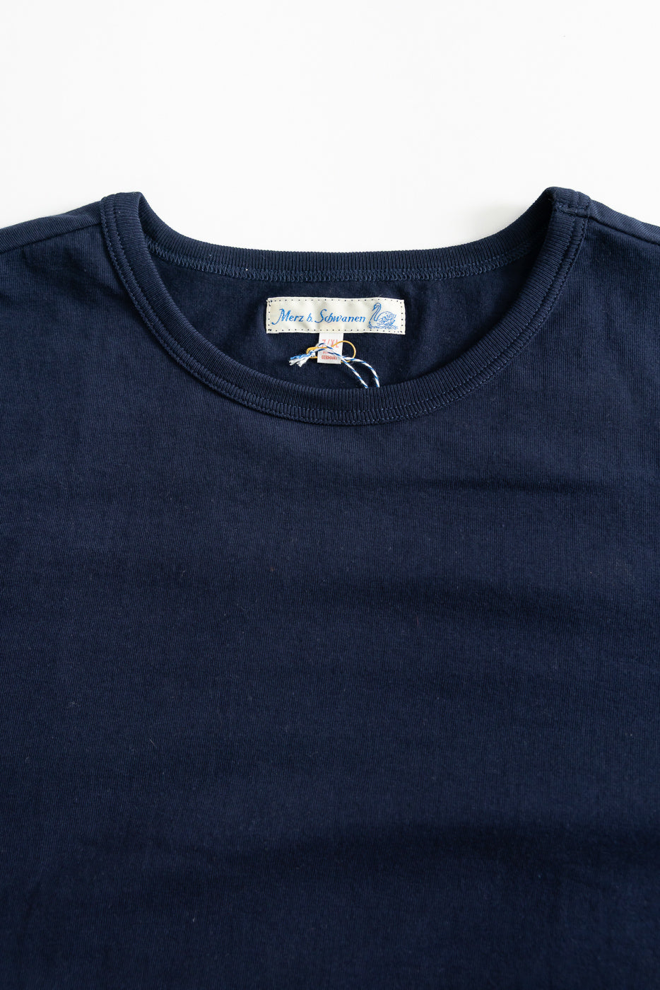 Close-up of the front upper chest and collar of an ink blue loopwheeled T-shirt, showing fabric texture, ribbed crew neck, and visible tag details.