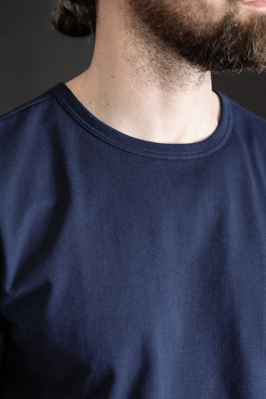 Close-up of male model's upper chest wearing ink blue crewneck t-shirt, showing fabric texture and classic collar, model is 5'9